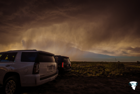 A white SUV and black SUV are parked to the left of the image with a stormy landscape and pouring rain featuring in the background