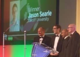 Jason on stage collecting the AOP Student of the Year Award - a screen with his face and name appear under the word "Winner" is shown behind him